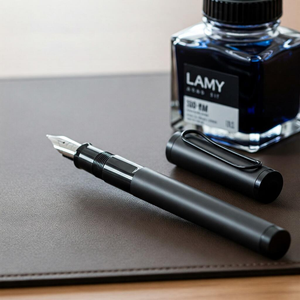 A close-up of the sleek and elegant Lamy Joy fountain pen, showcasing its smooth nib and high-quality design, placed on a wooden desk next to an ink bottle, highlighting its superior writing performance.