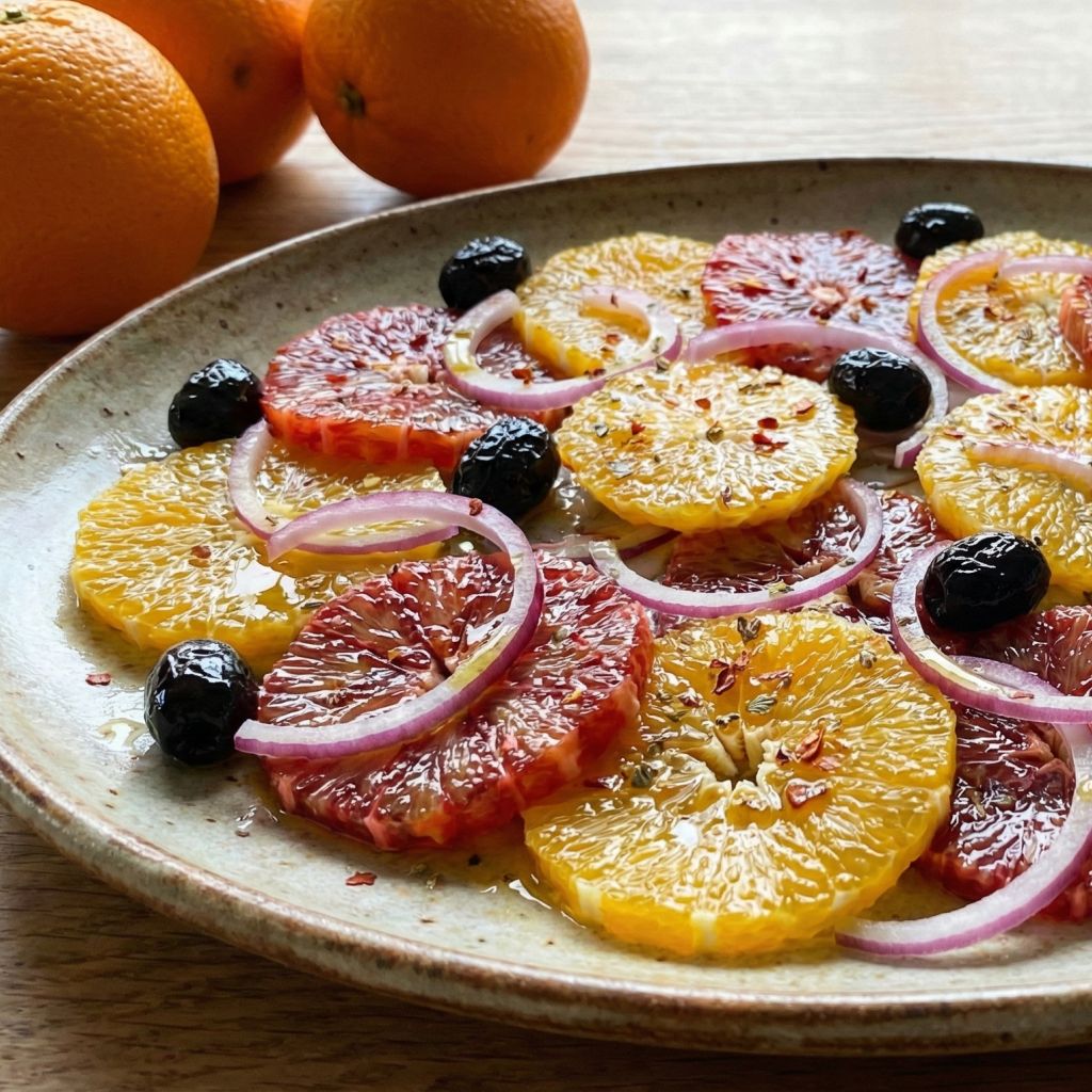 Vibrant Calabrian salad with sliced oranges, red onions, and black olives, seasoned with chili flakes and oregano on a rustic plate.