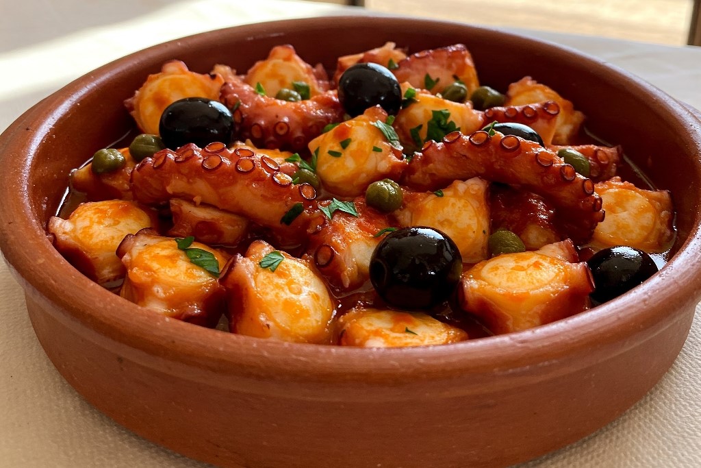 A plate of octopus alla Luciana, featuring tender octopus, black olives, capers, and tomatoes, garnished with fresh parsley for a traditional Neapolitan dish.